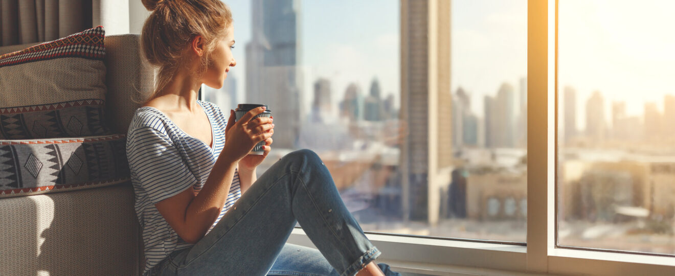 glückliche junge Frau trinkt morgens am großen Fenster Kaffee