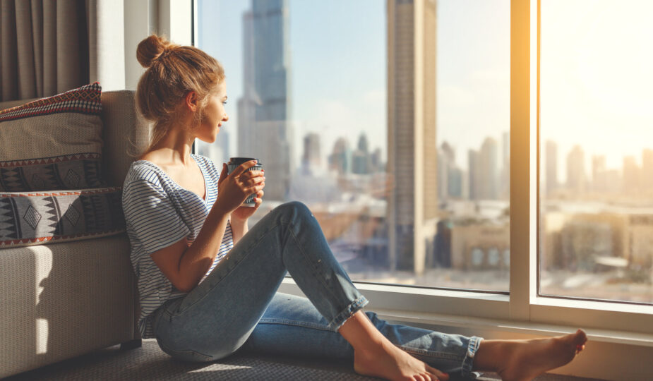 glückliche junge Frau trinkt morgens am großen Fenster Kaffee