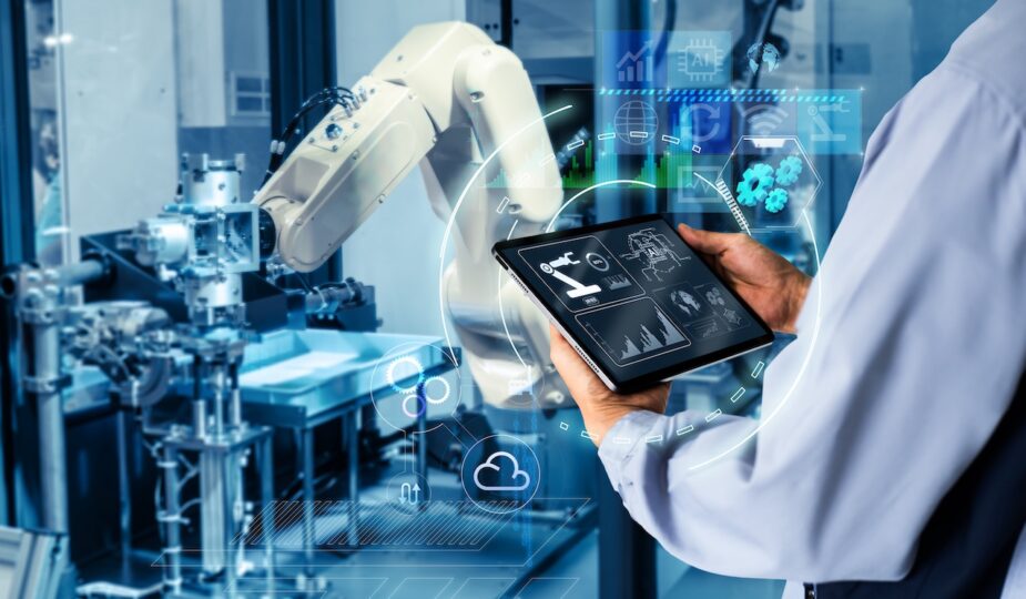 Mitarbeiter nutzt ein Tablet zur Steuerung eines automatisierten Roboterarms in einer digitalen Lagerhalle.