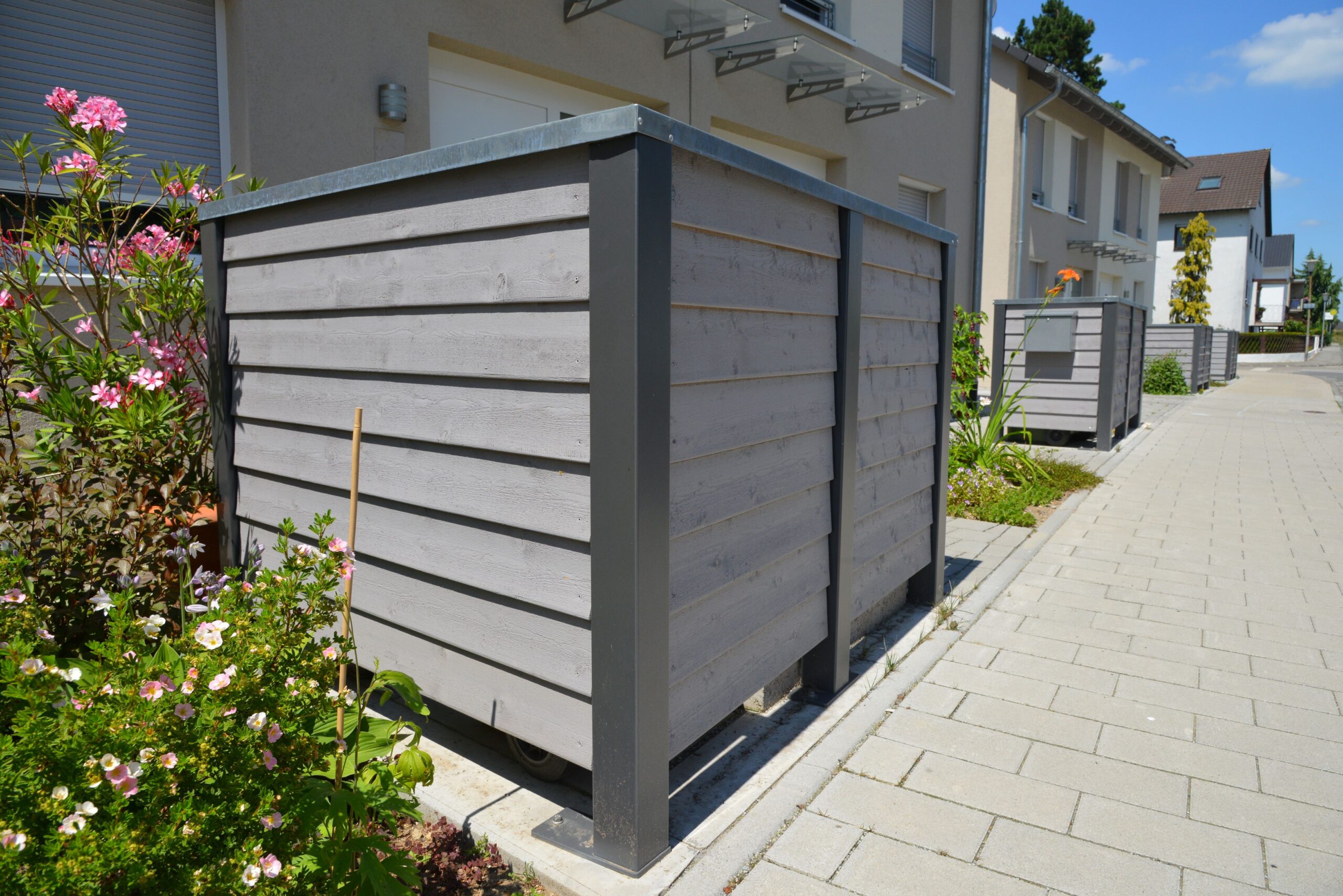 Mülltonnenbox aus Holz und Metall in Reihenhaussiedlung mit gepflegtem Vorgarten