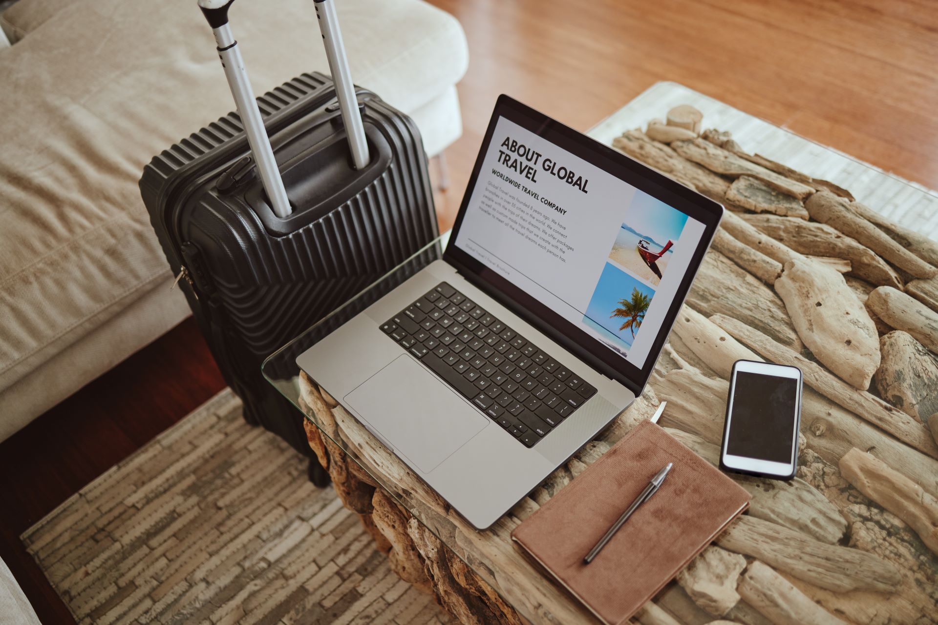 Laptop mit Reiseplanung neben Koffer und Notizbuch
