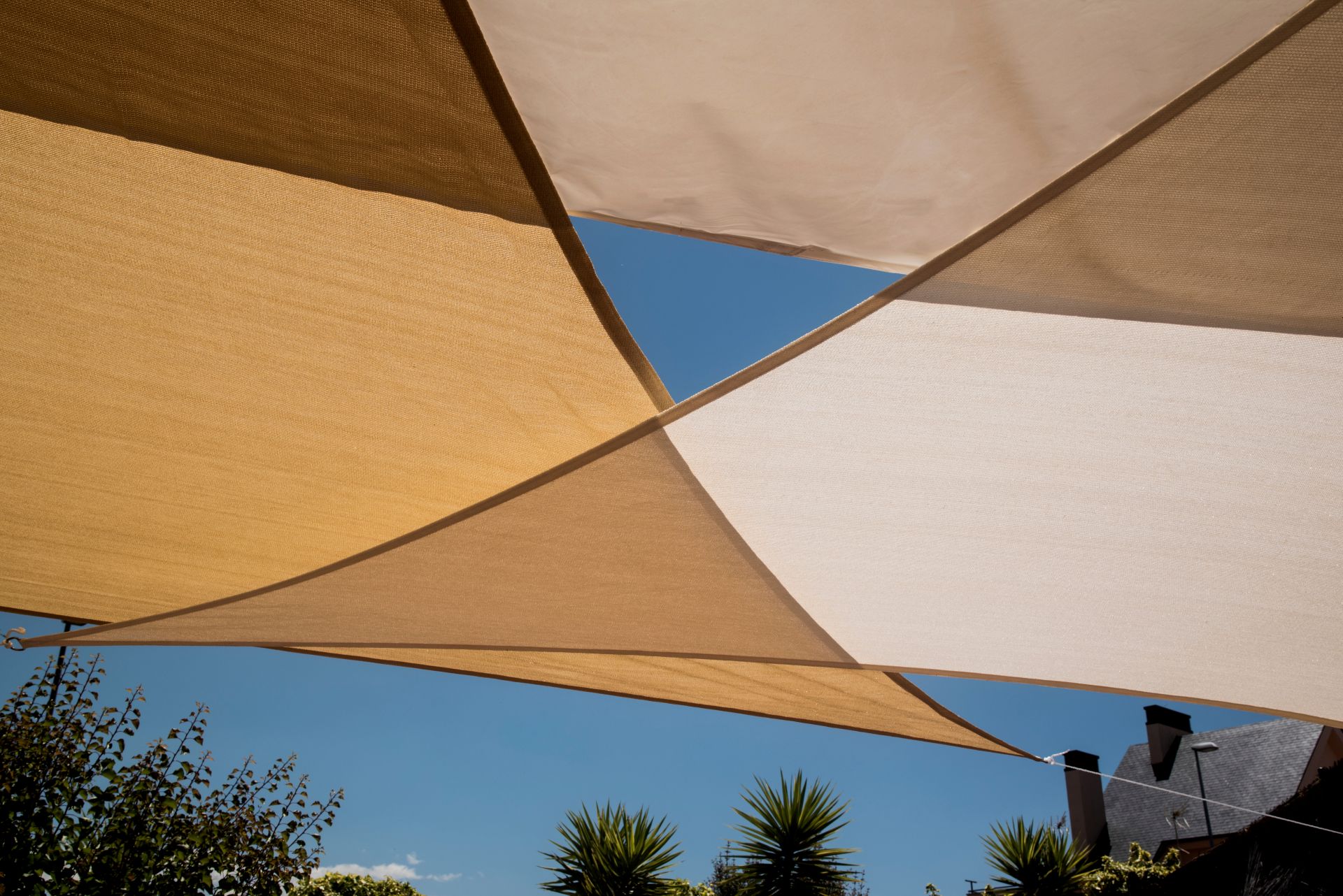 Mehrere beige Sonnensegel, die über einer Terrasse gespannt sind – funktionaler und stilvoller Schutz vor Sonne.